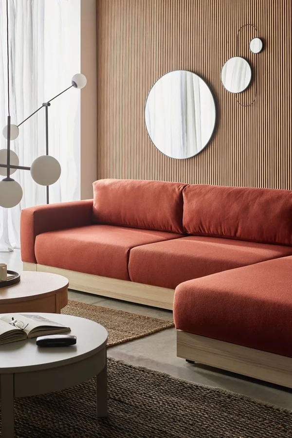 Przytulny salon z ceglastą sofą, lamelową ścianą i designerskimi lustrami.
